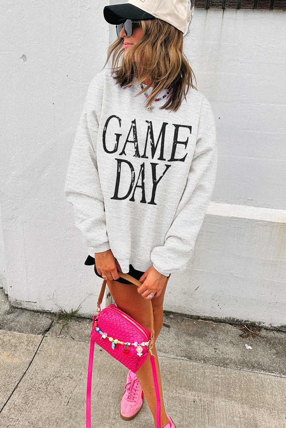Person wearing a 'GAME DAY' sweatshirt with a pink bag and pink sneakers against a white wall.