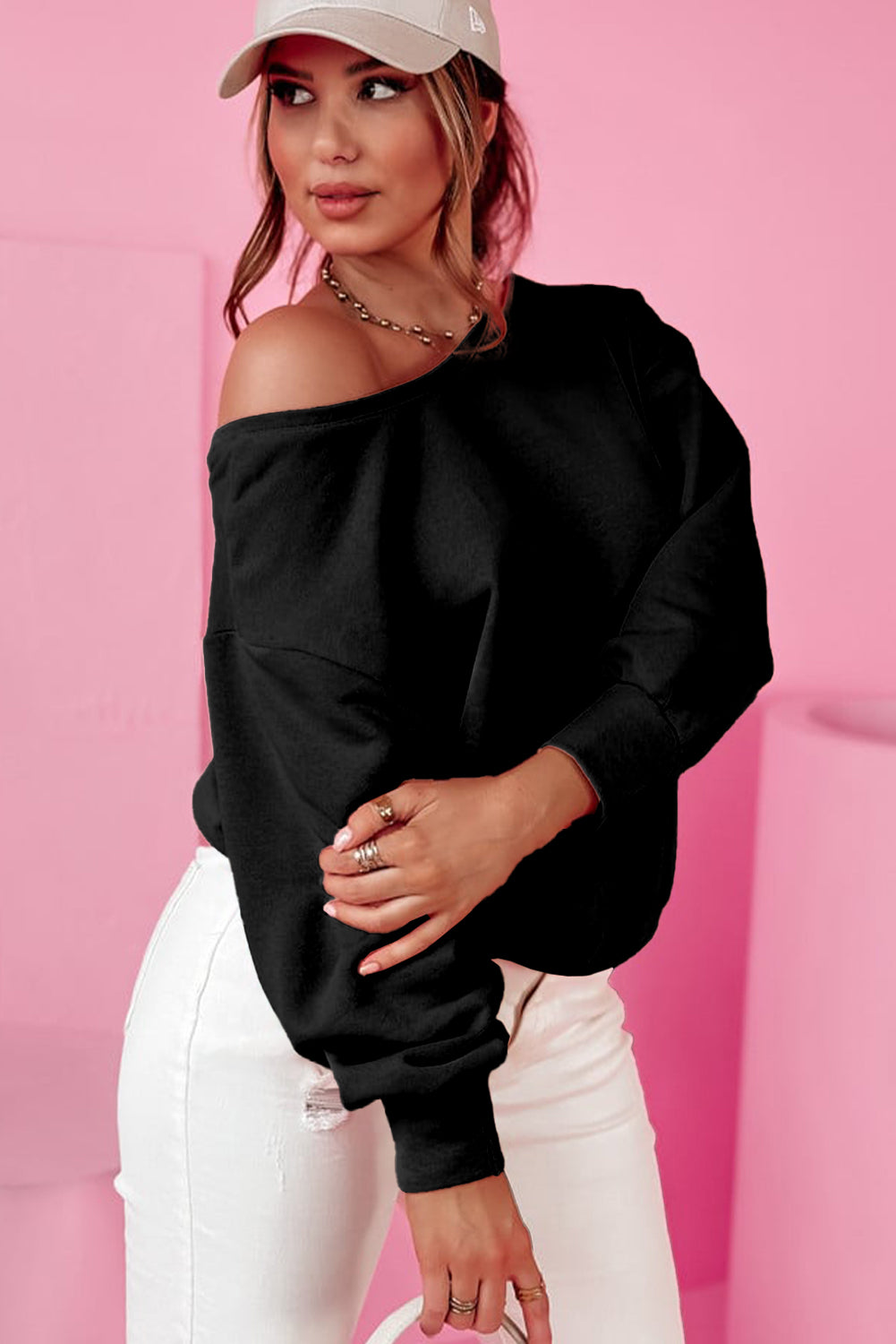 Woman wearing a black off-shoulder top and white pants against a pink background