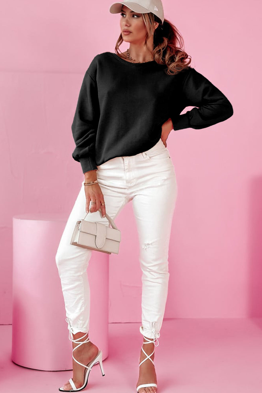 Woman wearing a black sweater, white pants, and high heels against a pink background