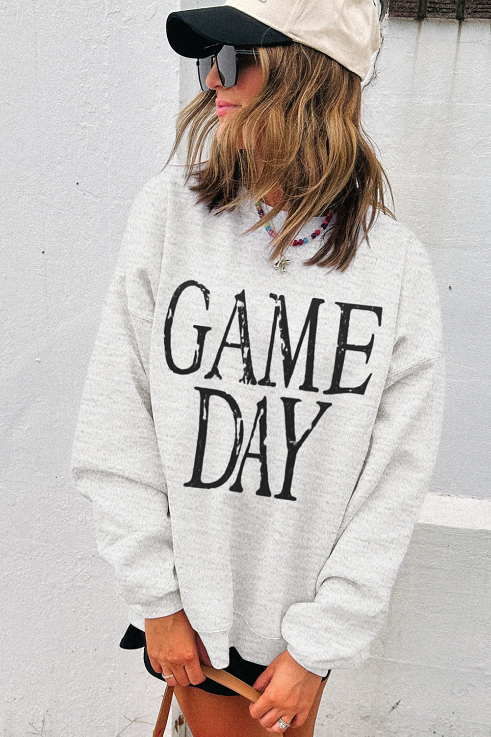 Person wearing a gray sweatshirt with 'GAME DAY' text against a white wall.