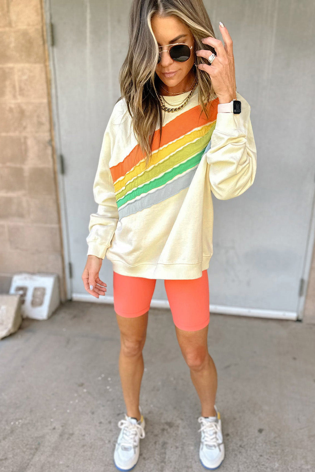 Woman wearing a colorful striped sweatshirt and bright orange shorts outdoors.